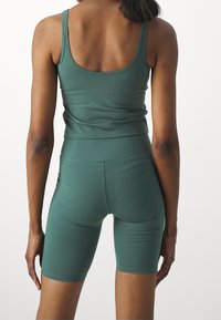 Mörkgrön sportig linne och shorts-set, tillverkat av elastiskt tyg. Har en figurnära design och en jämn textur.