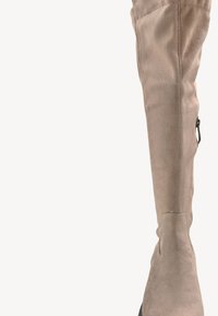 Beżowy zamszowy but do kolan o dopasowanym kroju, z bocznym zamkiem błyskawicznym i teksturowanym wykończeniem. Posiada płaską czarną podeszwę i minimalne akcenty.