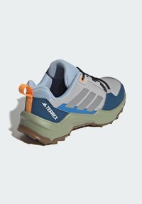 Lyseblå og grå atletiksko med mørkeblå accenter, tekstureret overdel, sorte snørebånd, orange træktab og en klodset grøn ydersål.