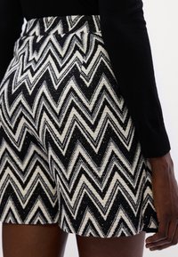 Pantaloni shorts neri e bianchi a motivo a zigzag realizzati in tessuto testurizzato, con vita aderente e design a bordo ondulato.