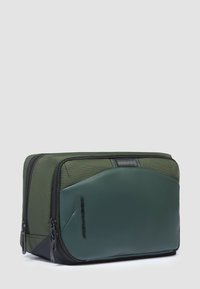 Bolsa verde con exterior de tela texturizada y detalles en cuero suave. Doble cremallera y diseño minimalista con una marca sutil.