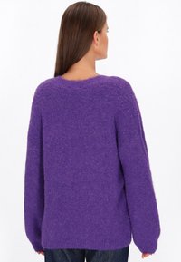 Maglione viola, oversize, con una consistenza morbida, scollatura tonda e maniche lunghe, leggermente affusolate. Presenta un design della schiena senza cuciture.
