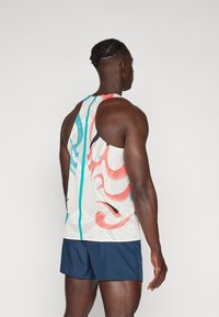 Hvid tanktop med farverige abstrakte mønstre i rød, blå og sort. Har en racerback-design og struktureret stof. Kombineret med marineblå shorts.