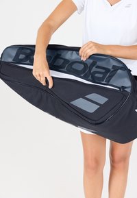 Borsa sportiva nera con un grande logo grigio, dotata di chiusura con zip e bordi rinforzati, tenuta aperta per rivelare la fodera interna.
