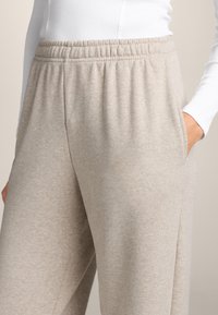Lichtbeige sweatpants met een zachte textuur, elastische tailleband, zijzakken en een casual pasvorm, gedeeltelijk weergegeven tegen een neutrale achtergrond.