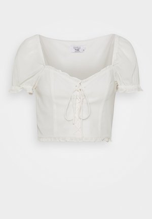 Blouse courte blanche avec manches courtes bouffantes, encolure carrée, devant lacé et ourlet et bords de manches volantés.