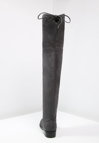 Gray over-the-knee boot made of soft leather with a rounded toe, subtle stitching details, and a back lacing system for a custom fit.
