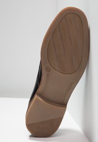 Černá podrážka boty s texturovanou hnědou gumovou základnou, která má vodorovné a svislé drážky pro trakci a tvarovaný design.