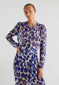 Set di blusa e vestito trasparenti con un motivo leopardato blu, marrone e crema, dotato di collo alto, chiusura con bottoni e maniche lunghe.