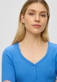 Blauw geribbeld brei-t-shirt met korte mouwen, V-hals en vijf blauwe knopen aan de voorkant, met een gladde textuur en een aansluitend ontwerp.