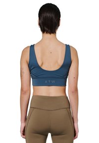 Blå sportsbh med brede stropper, scoop ryg og "ATW" logo i grå. Glat, strækbart stof parret med brune højtaljede leggings.