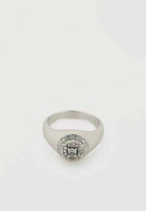 Srebrny pierścionek Guess z okrągłym skupiskiem przezroczystych kryształów i wygrawerowaną nazwą marki otaczającą centralny kamień.