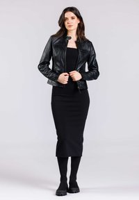 Giacca in pelle nera dal design aderente e colletto rialzato, abbinata a un vestito bodycon nero e stivali al ginocchio. Tessuto liscio, aspetto elegante.