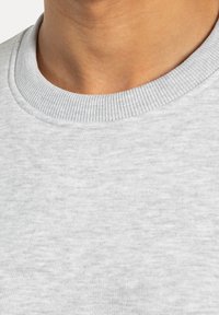 Tessuto di felpa grigio chiaro con colletto a girocollo testurizzato e rigato, superficie liscia che mostra lievi variazioni di colore e trama.