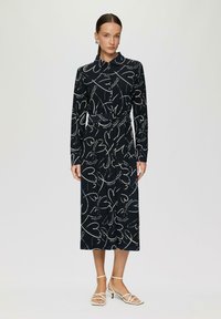 Abito con maniche lunghe e bottoni in tessuto blu navy con stampa a cuori bianchi. Dotato di una vita con cintura e gonna dritta. Tacchi bianchi con cinturini.