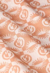 Katoenen stof met een perzikkleurige achtergrond en een herhaald patroon van lachende gezichten en gestileerde zonnestralen in off-white.