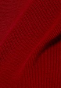 Gros plan sur un tissu tricoté rouge côtelé montrant sa texture et ses légers plis.