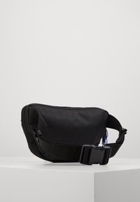 Zwarte stoffen heuptas met een verstelbare band en een sluitgesp, rustend op een witte ondergrond tegen een effen achtergrond.