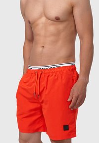 Shorts de bain orange vif en tissu léger, dotés d'une taille élastique avec cordon de serrage et d'un petit patch logo noir.