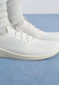 Weiße SportSneaker mit einem Obermaterial aus Mesh, strukturiertem Oberflächenfinish und einer flexiblen Gummisohle. Die Schnürsenkel sind vorne gesichert, im minimalistischen Design.