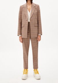 Brun och beige rutig kostym med dubbelknäppt kavaj och skräddarsydda byxor, tillsammans med vita sneakers och gula snören.