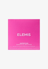 Boîte rose étiquetée "ELEMIS SUPERFOOD ESSENTIAL ROUTINE", avec du texte blanc et des détails sur les produits inclus. Texture lisse et brillante.