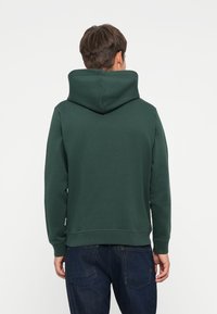 Hoodie vert foncé en tissu doux, avec une grande capuche et des poignets côtelés. Le design présente une coupe décontractée et un style minimaliste.