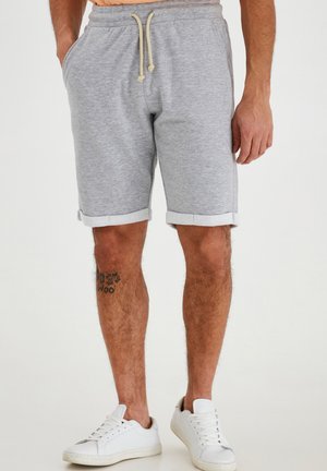 Pantalones cortos de mezcla de algodón grises con cintura ajustable, dobladillo vuelto, bolsillos laterales y combinados con zapatillas blancas. Presenta un tatuaje en la pierna.