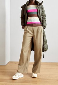 Puffjacka i olivgrön, randig tröja i rosa, blå, beige och brun, beige vida byxor och krämfärgade sneakers med gula detaljer.