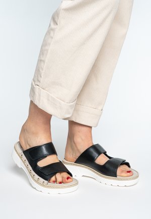 Black leather slide sandals with two wide straps, featuring a chunky white sole with raised texture and decorative studs along the side.