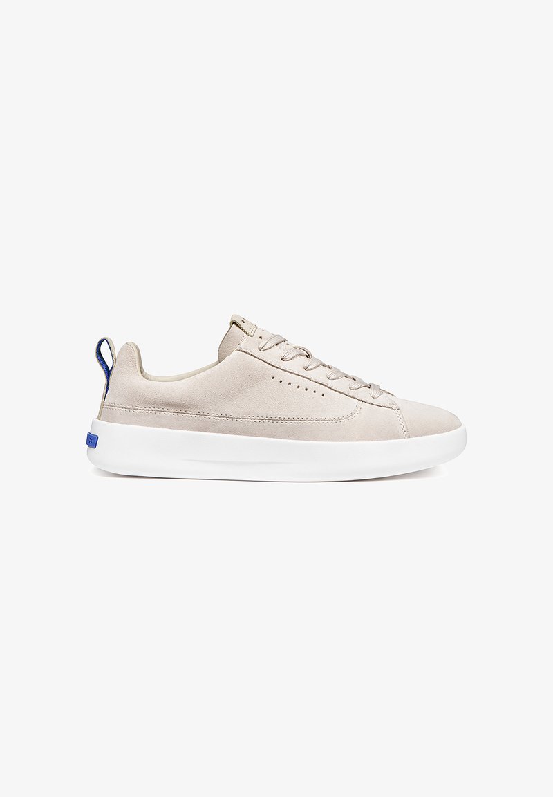 Baskets basses en daim beige avec semelle blanche épaisse, lacets à l'avant, et languette bleu au talon, vues de profil sur fond blanc.