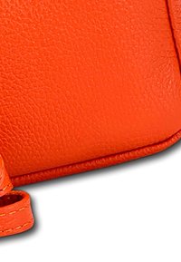 Oranger Lederbeutel mit strukturierten Oberfläche, ausgestattet mit einer genähten Kante und einer runden Tragegurtbefestigung. Kompaktes rechteckiges Design.