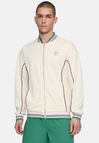 Krämsfärgad zip-up jacka med lila och gröna randiga ribbade kragar och manschetter. Har en subtil logotyp och sidopipingdetaljer. Mjuk textur.