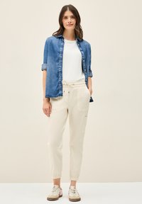 Lehká košile s knoflíky z chambray v modré barvě, bílý tričko a krémové tapered jogger kalhoty s elastickými náplety na kotnících a dvěma bočními kapsami.