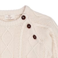 Cárdigan crema con un patrón de punto en relieve, que presenta tres botones marrones oscuros en el hombro y un cuello acanalado.