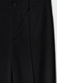 Zwarte op maat gemaakte trousers van een gladde stof, met een gepolijste afwerking, voorplooien en een enkele knoopsluiting.