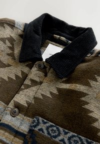 Giacca di lana marrone a fantasia con colletto in velluto a coste scuro e grandi bottoni, posata piatta che mostra la parte anteriore superiore e l'etichetta all'interno del colletto.