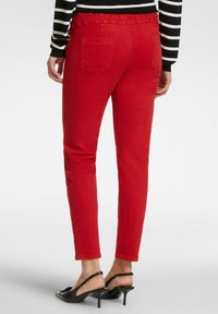 Jeans rojos de corte Slim, diseño de cinco bolsillos y cinturilla. Combinados con tacones negros tipo slingback. El material parece ser denim.