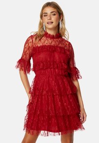 Abito rosso in pizzo con design a strati, maniche corte con volant, scollatura alta e tessuto trasparente. Dettagli eleganti e intricati.