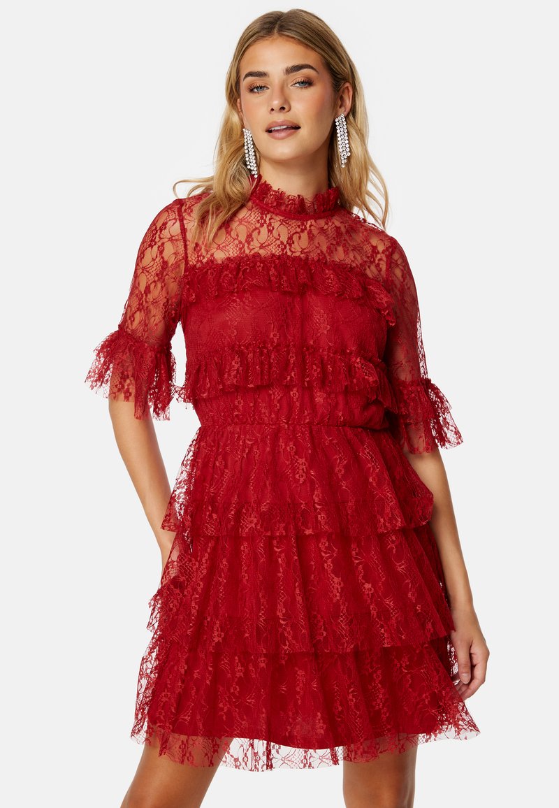 Abito rosso in pizzo con design a strati, maniche corte con volant, scollatura alta e tessuto trasparente. Dettagli eleganti e intricati.