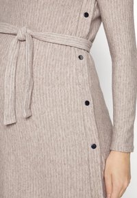 Gestreiftes Strickkleid in Hellbeige mit einem gebundenen Taillengürtel, ausgestattet mit schwarzen Knöpfen entlang der Seite und einem strukturierten Stoff.