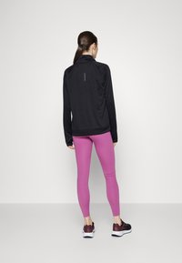 Una giacca sportiva nera con colletto alto è abbinata a leggings rosa aderenti. Le calzature sono scarpe da ginnastica nere e bordeaux.