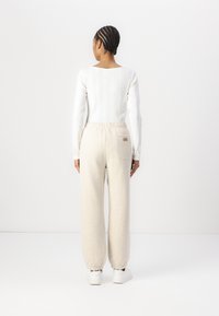 Leichter, weißer, gerippter Langarm-Top kombiniert mit hoch taillierten, cremefarbenen Sweatpants mit elastischen Bündchen und einer Gesäßtasche.
