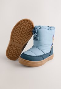 Blaue Stiefel mit gepolstertem Obermaterial, gummierter Außensohle und orangefarbener Sohle. Die Seite zeigt eine Charaktergrafik mit einer glatten, glänzenden Textur.