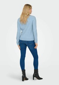 Maglione lavorato a maglia di un blu chiaro con maniche lunghe, abbinato a jeans skinny blu scuro e stivaletti neri con tacco, visti da dietro.