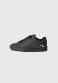 Svart lädersneaker med rund tå, perforerad detaljering och fyra snörhål. Har en svart gummisula och en silverfärgad logotyp. 