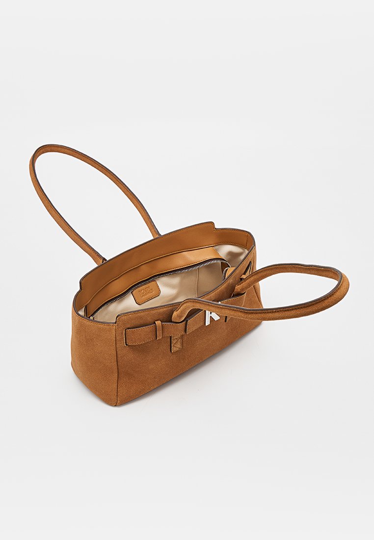 Bolso de hombro de ante marrón con ribete de cuero, parte superior abierta que muestra el forro interior beige y un bolsillo con cremallera en el interior.