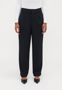 Black tailored trousers with a high waist, pleats, and side pockets. Made of smooth fabric, with a button closure and cuffed hems.