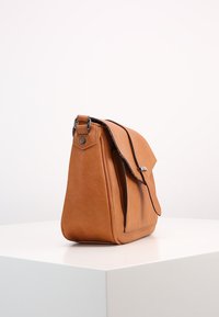 Ruskea nahkainen olkalaukku, jossa on läppäkiinnitys, sileä pinta ja hopeanväriset yksityiskohdat. Laukku on kolmionmuotoinen ja siinä on sivutasku.