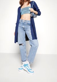 Ljusblå paljettbeströdd crop top, marinblå kofta, slitna ljusblå jeans och blåvita sneakers. Accessoarer inkluderar en liten blå väska.